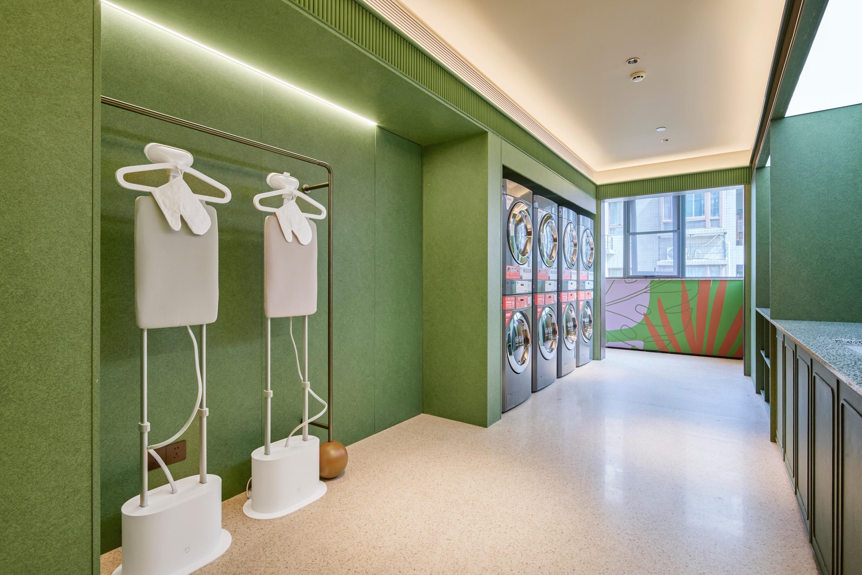 A hallway with green walls, a tiled floor, and a row of washing machines.