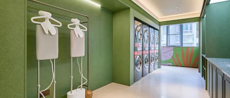 A hallway with green walls, a tiled floor, and a row of washing machines.