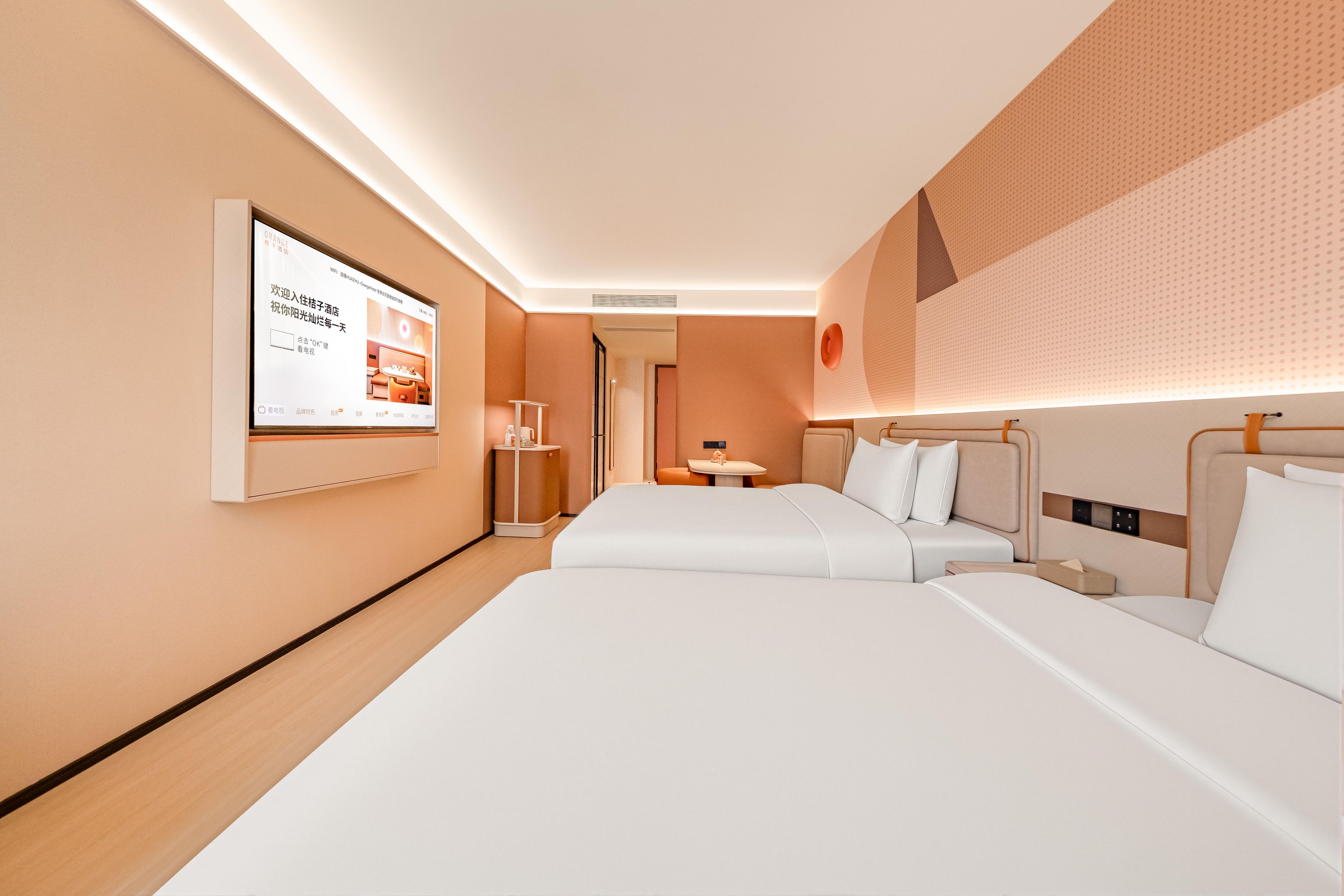 Habitación de hotel con dos camas, un televisor de pantalla plana montado en la pared y una mesita de noche con lámpara.