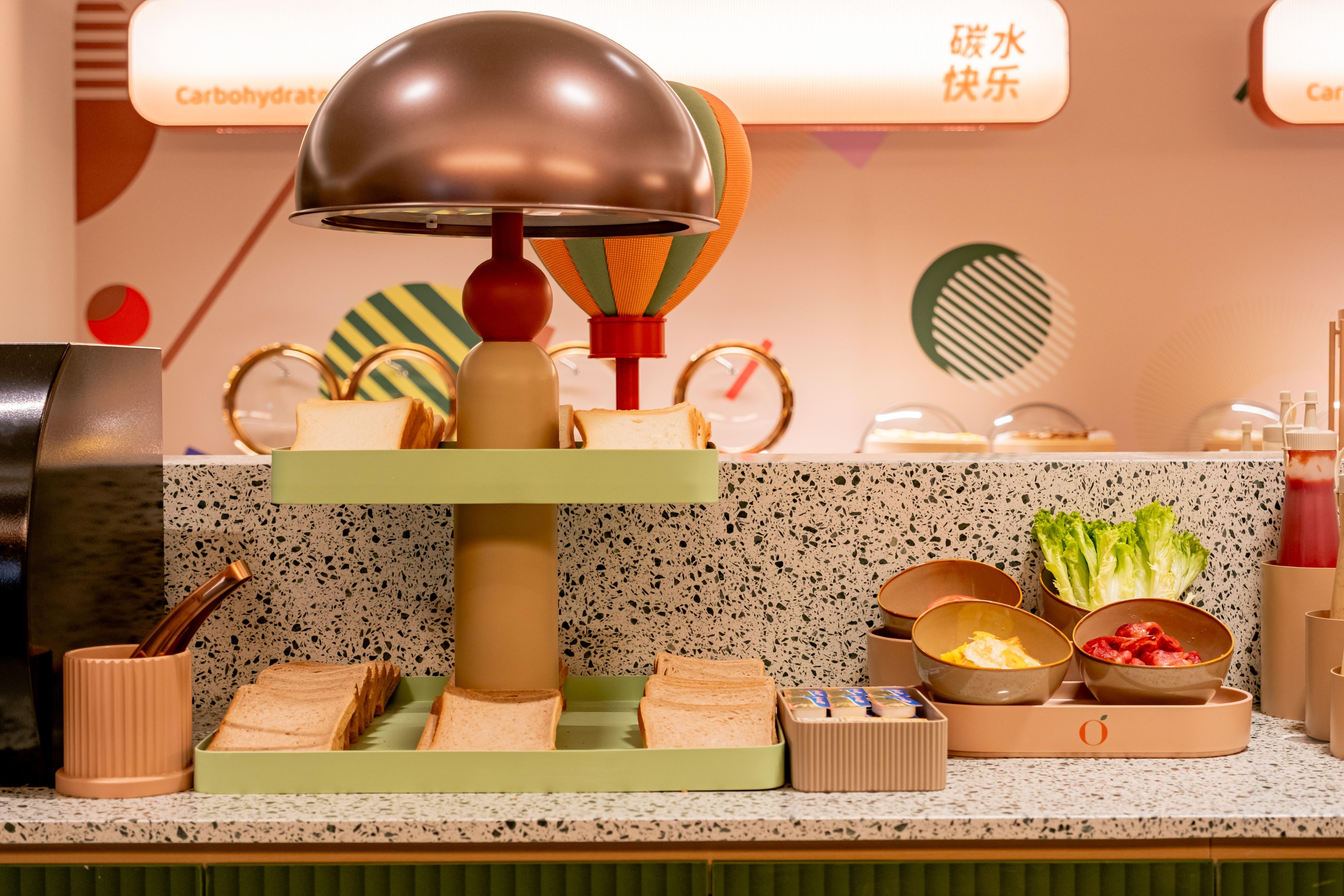 A kitchen counter with a bread-making machine, various bread loaves, condiments, and a clock.