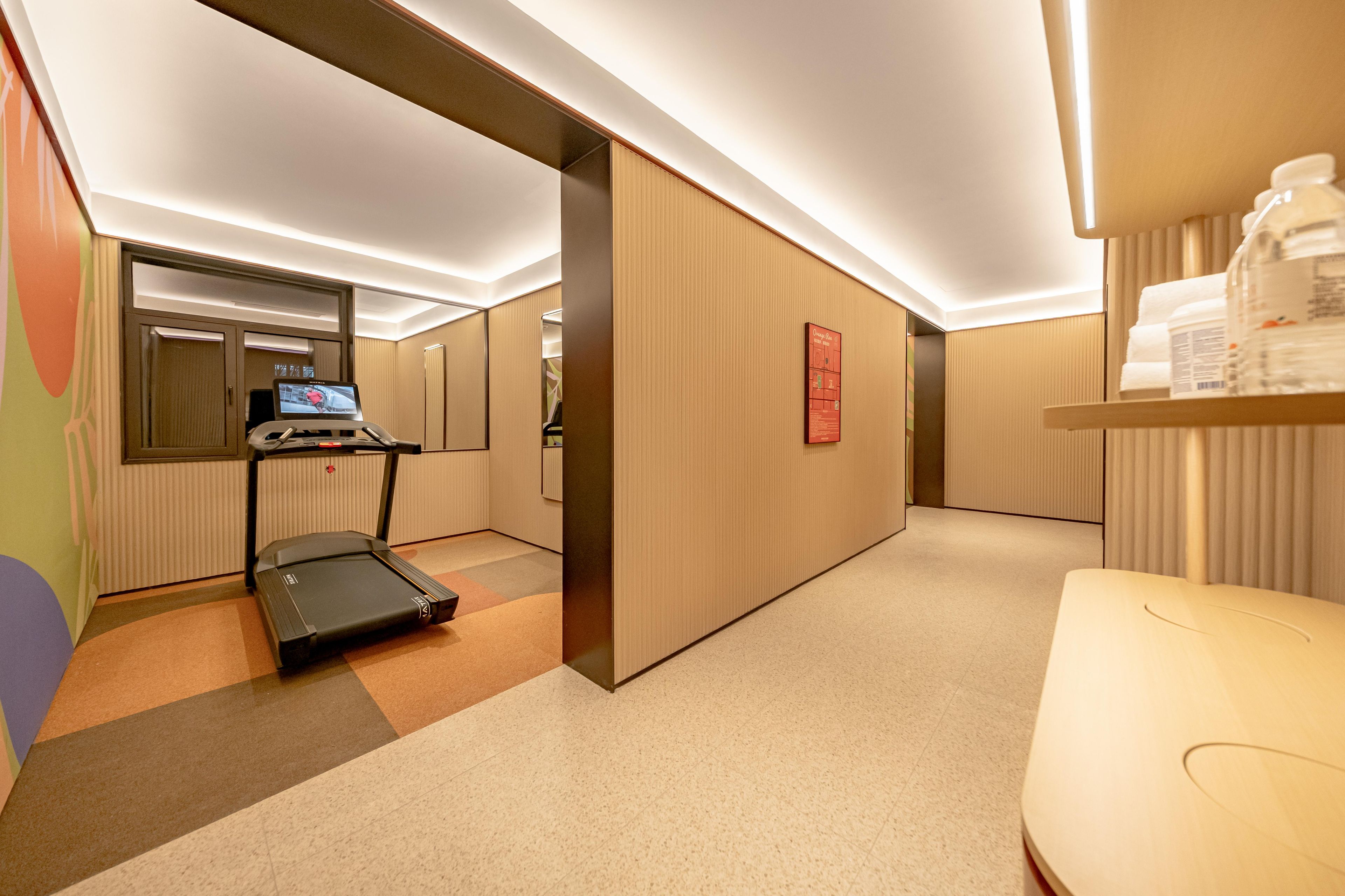 A hotel room with a treadmill, a small desk, and a wall-mounted TV.