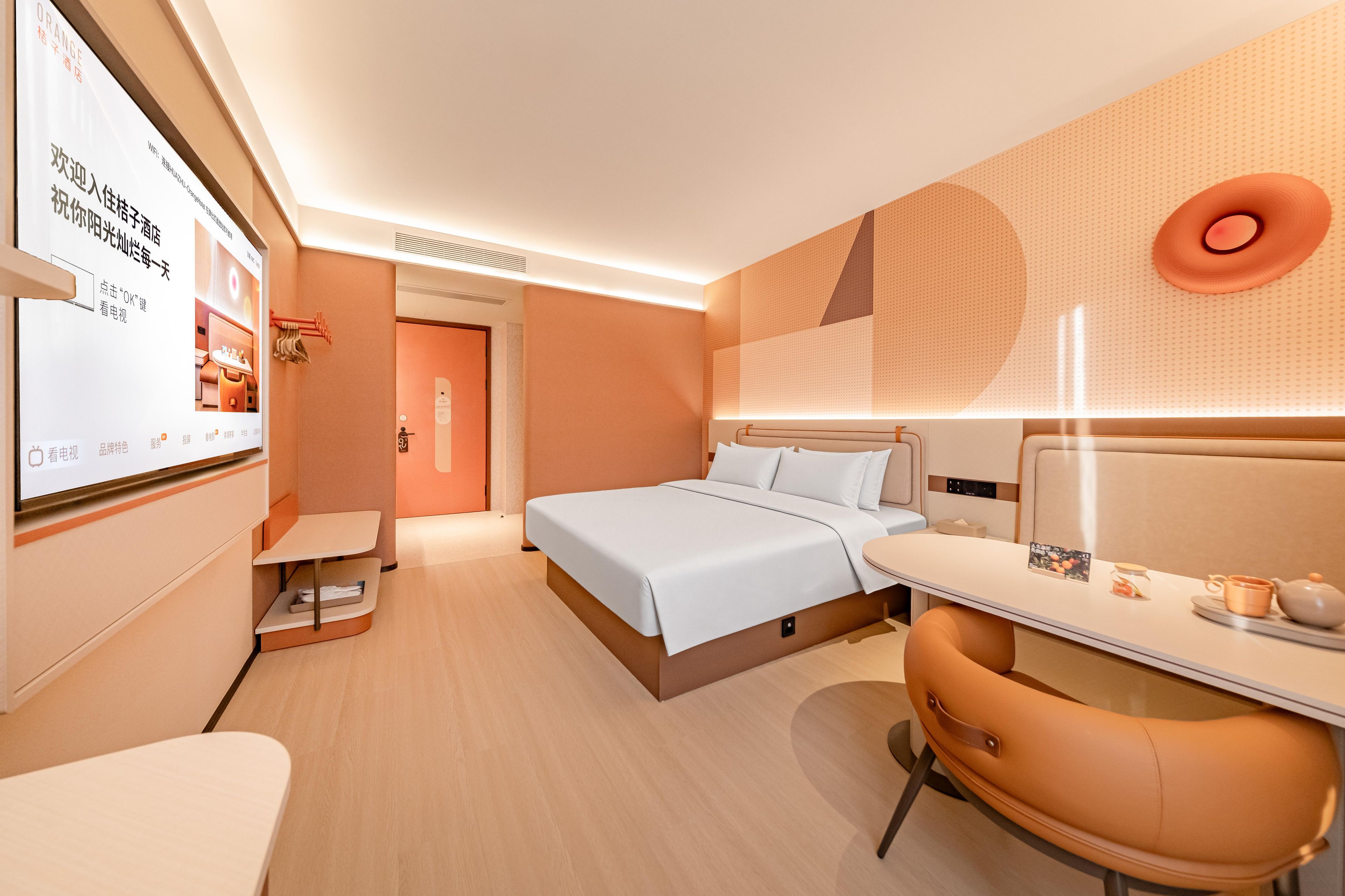 A modern hotel room with a bed, bedside table, chair, and a desk with a computer.