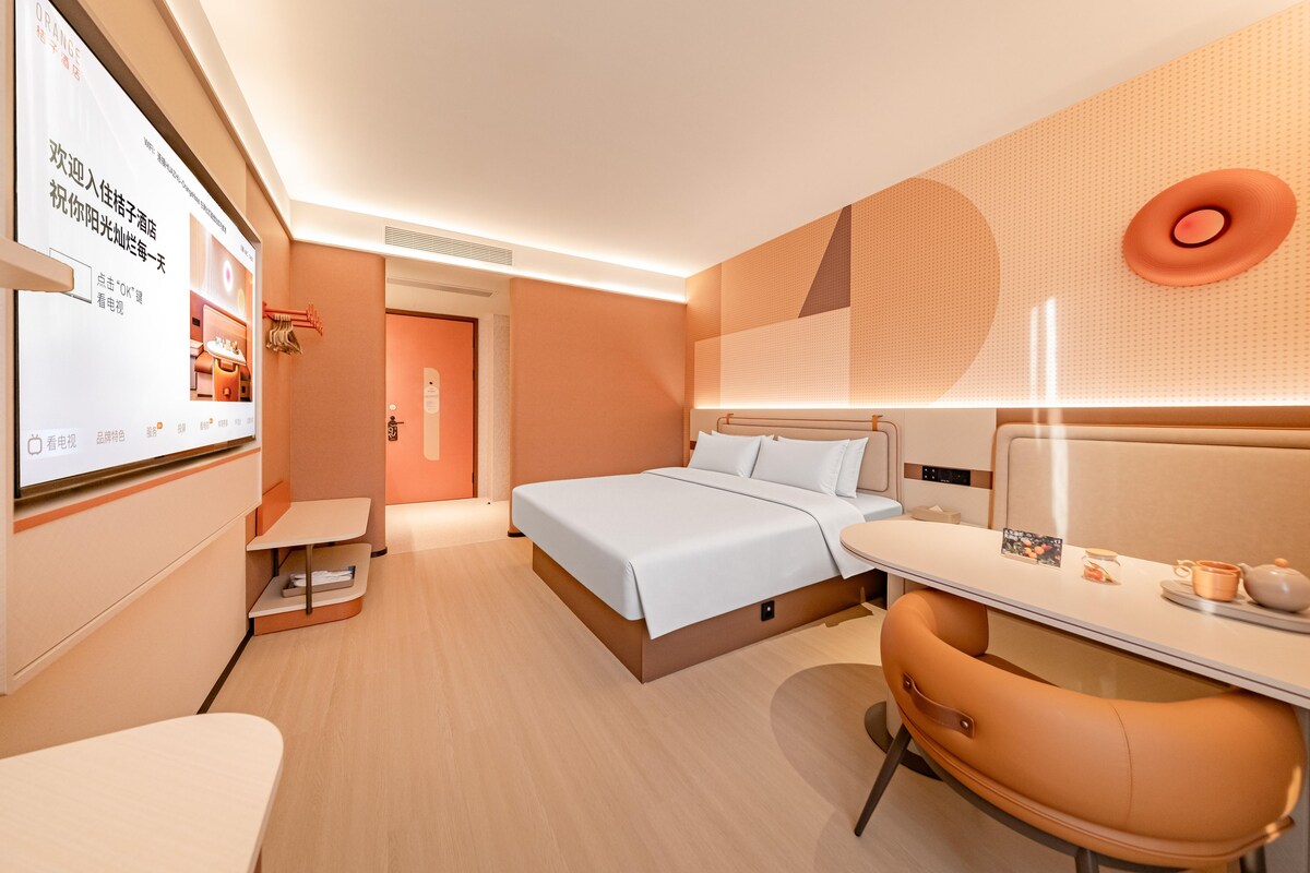 A modern hotel room with a bed, bedside table, chair, and a desk with a computer.