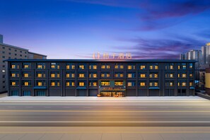 Un moderno edificio alberghiero con diversi piani, ampie finestre e un cartello al neon ben visibile.