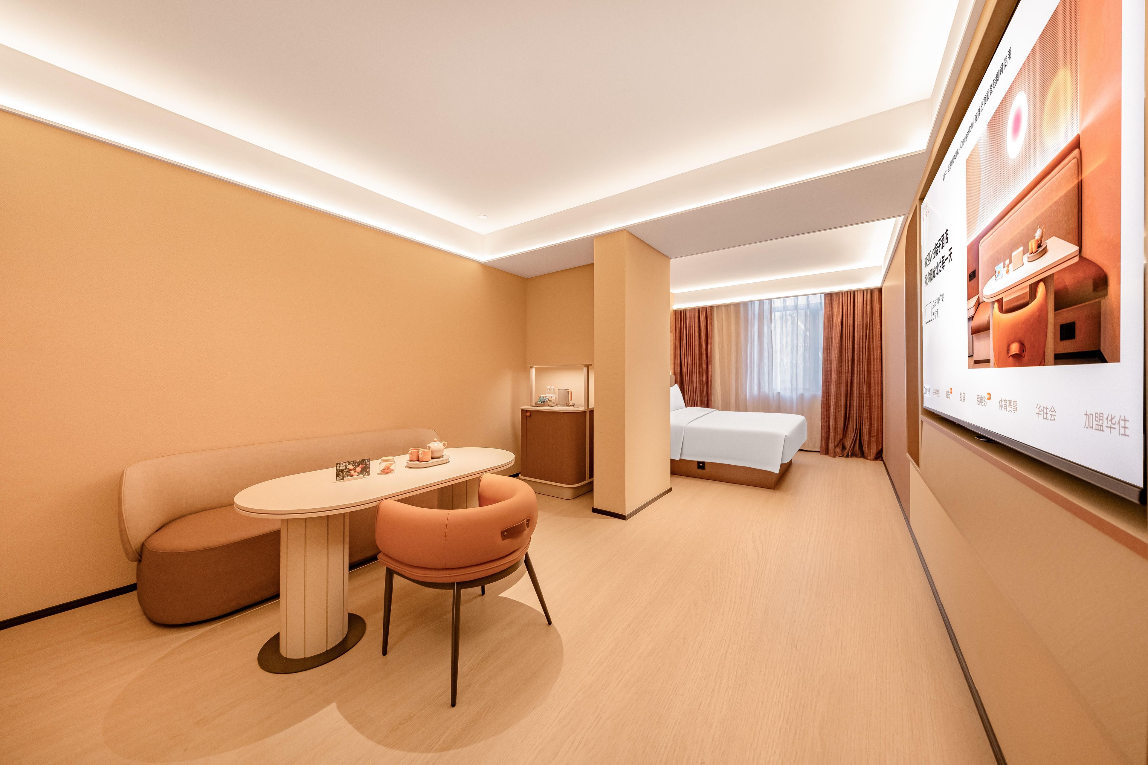 Quarto de hotel com uma cama, área de estar com uma mesa, televisão e mesa de cabeceira com abajur.