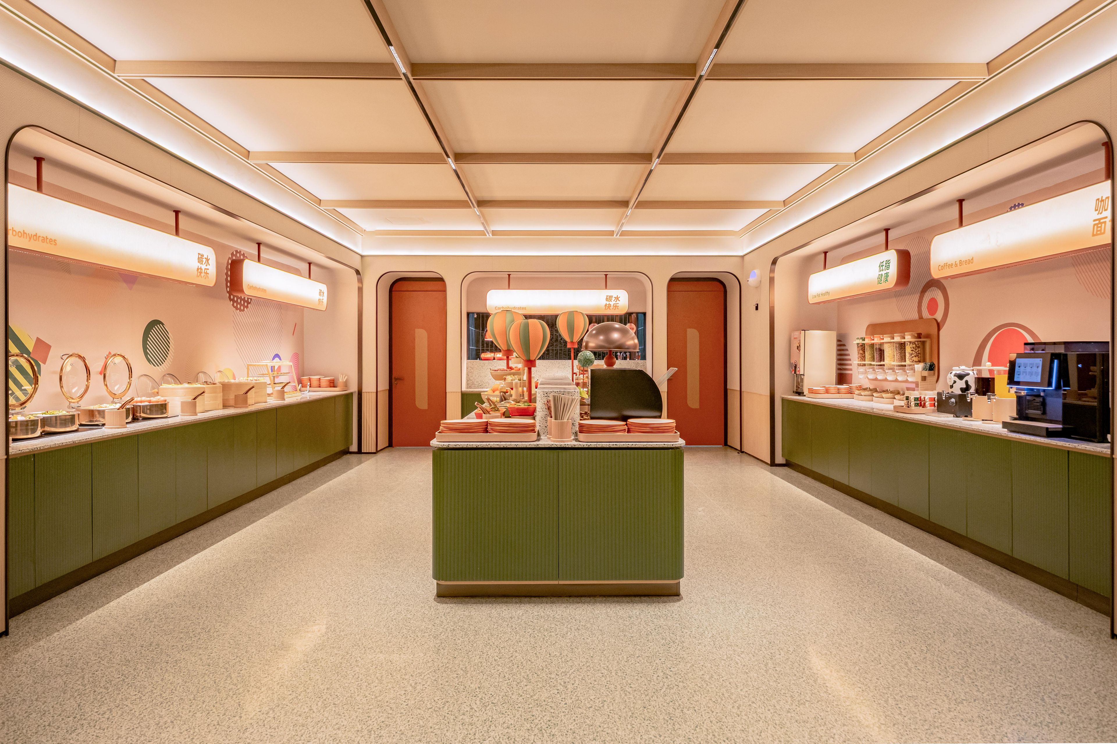 A modern, well-lit cafe with a central counter, green cabinets, and various food and drink items displayed.
