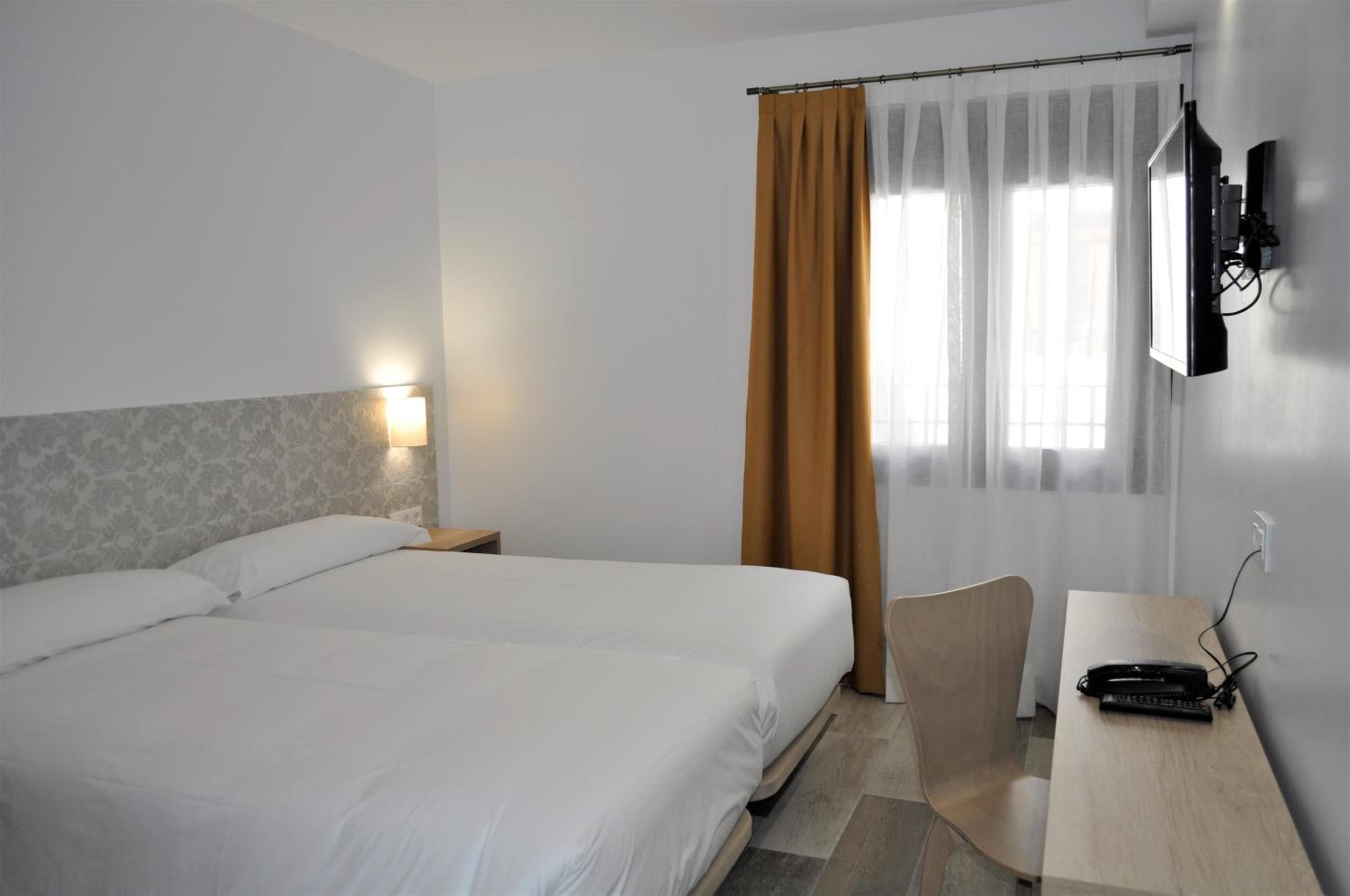 Habitación de hotel con cama doble, escritorio con teléfono, una silla, televisión montada en la pared y ventana con cortinas.