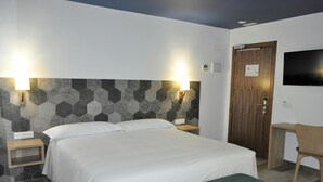A hotel room with a large bed, two bedside tables, a wooden door, a television on the wall, and a patterned wall. - Hostal Restaurante Villa De Brihuega (Brihuega)