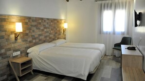 A hotel room with two beds, a desk, a chair, a TV, and a brick-patterned wall. - Hostal Restaurante Villa De Brihuega (Brihuega)