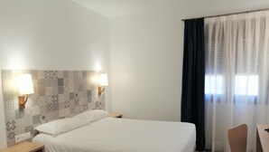 A hotel room with a large bed, two bedside tables, a desk with a chair, and a window with curtains. - Hostal Restaurante Villa De Brihuega (Brihuega)