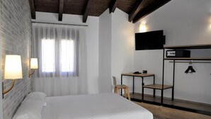 A hotel room with a bed, a desk, a chair, a television, and a coat rack. - Hostal Restaurante Villa De Brihuega (Brihuega)