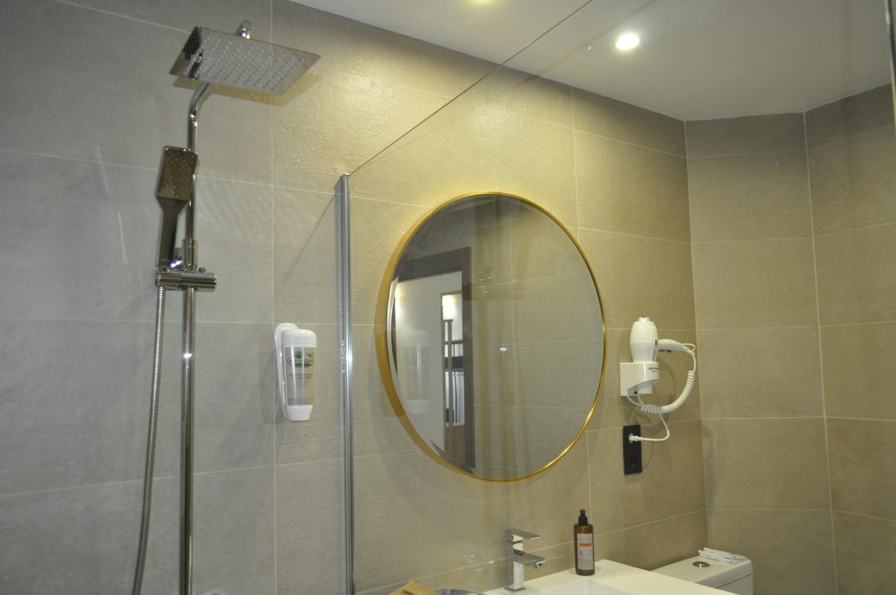 Ein Badezimmer mit Dusche, einem runden Spiegel, einem Fön und einem Waschbecken.