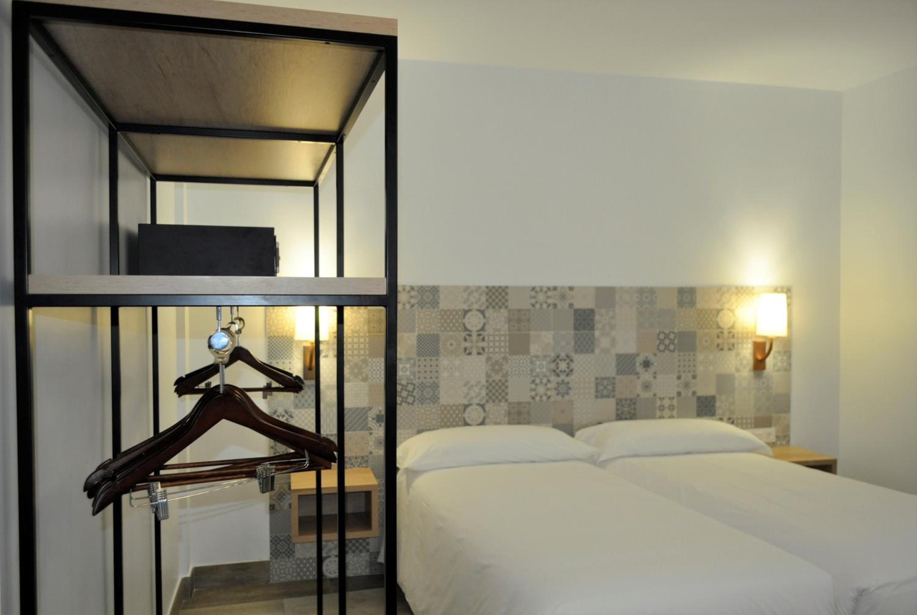 Una habitación de hotel con literas, una mesita de noche, una lámpara de pared y un papel tapiz estampado.