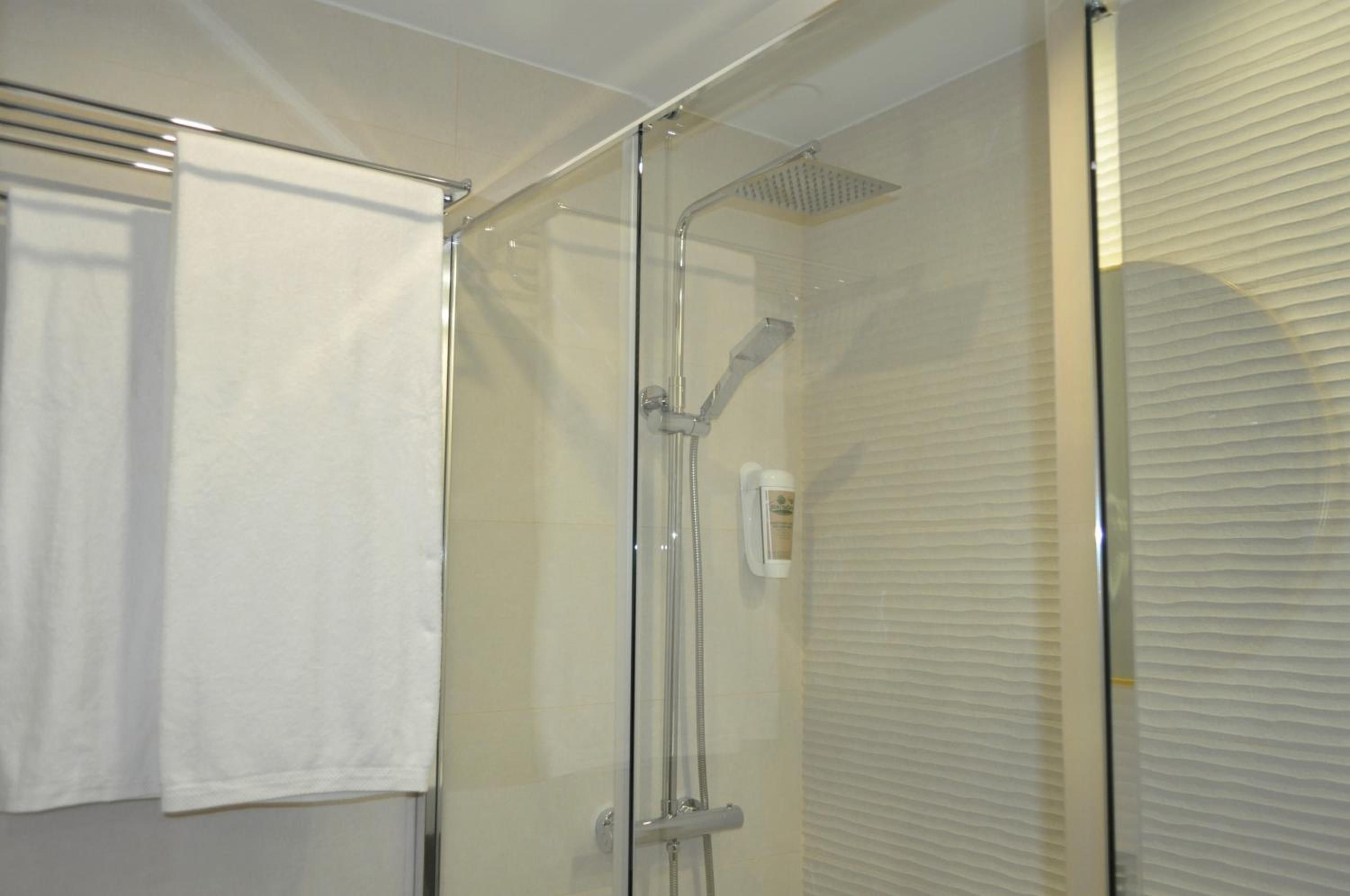 Cabina de ducha con paredes de vidrio, un cabezal de ducha manual y un panel de control en la pared.