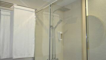 Cabina de ducha con paredes de vidrio, un cabezal de ducha manual y un panel de control en la pared.