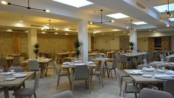 Un amplio comedor con varias mesas y sillas, una pared de piedra y modernas luminarias.