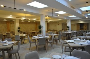 Un amplio comedor con varias mesas y sillas, una pared de piedra y modernas luminarias.