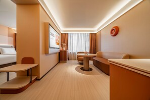 A hotel room with a bed, a desk, a sofa, a small table, and a TV mounted on the wall. - Orange Hotel (Xi'an)