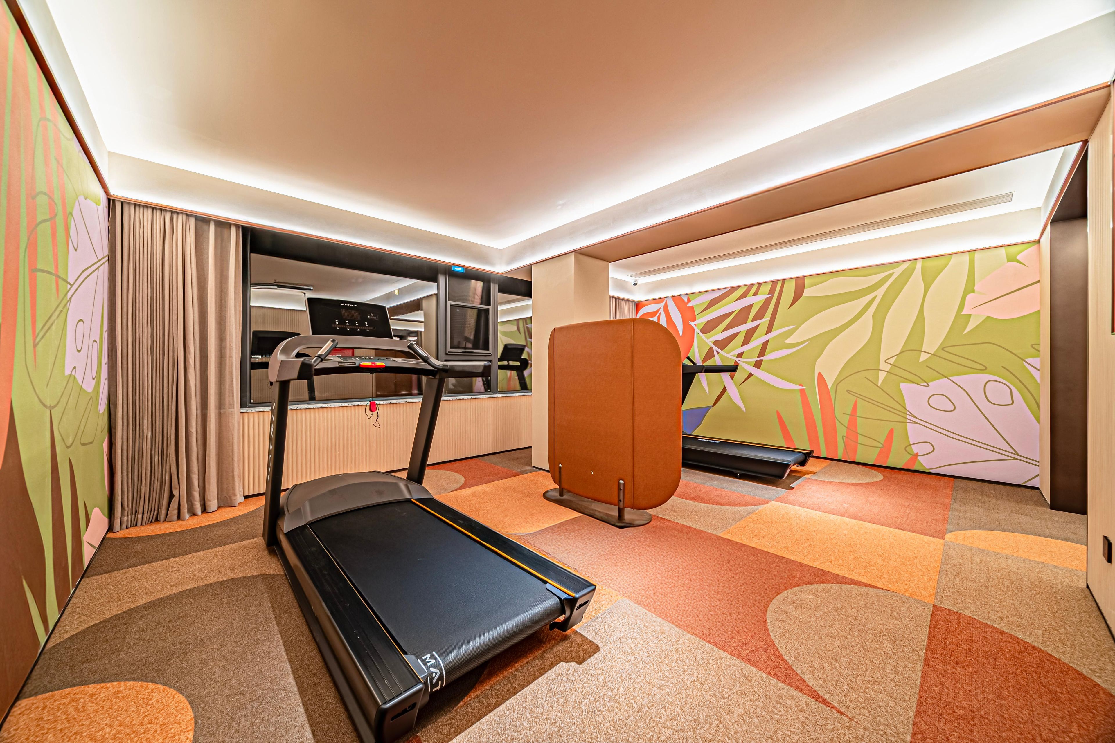 A hotel room with a treadmill, exercise equipment, a television, and a large window.