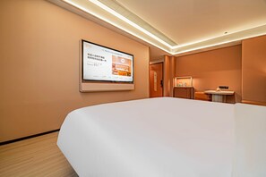 Una habitación de hotel con una cama grande, una mesita pequeña, un televisor montado en la pared y una puerta que da a otra habitación.