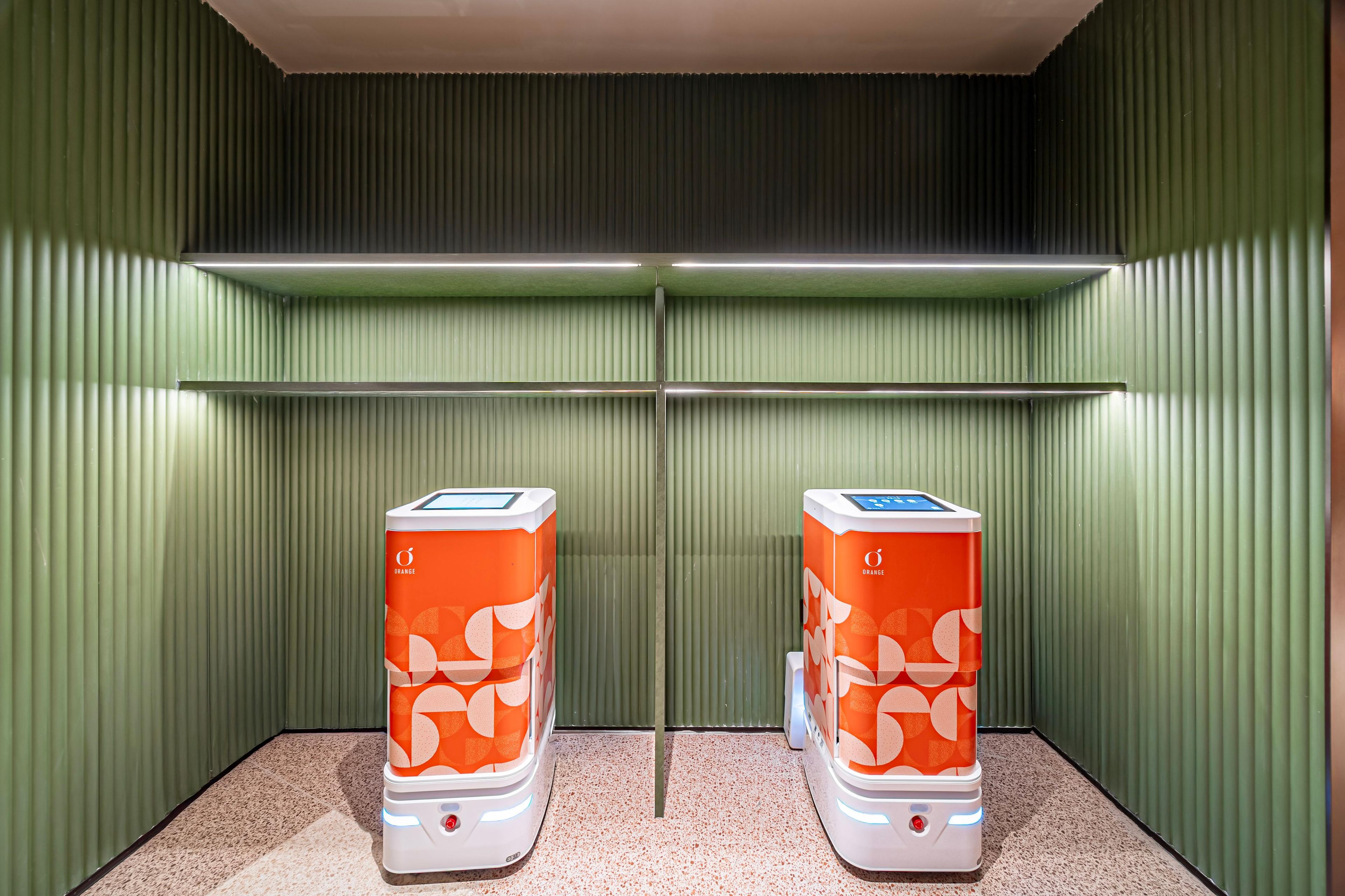 Two orange self-service kiosks in a room with green walls and a speckled floor.