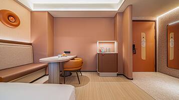 A modern hotel room with a sofa, a small table, a cabinet, and a door.