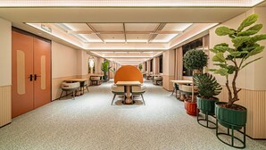 A modern hotel corridor with a central seating area, potted plants, and a clear exit sign.