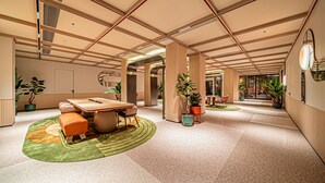 A spacious lobby with a high ceiling, a central seating area with a table and chairs, and potted plants. - Orange Hotel (Xi'an)