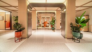 A modern hotel lobby with a central corridor, potted plants, and a seating area. - Orange Hotel (Xi'an)