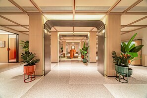 A modern hotel lobby with a central corridor, potted plants, and a seating area. - Orange Hotel (Xi'an)