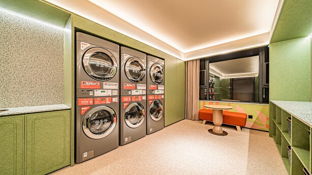 A laundry room with four washing machines, a sink, and a mirror.