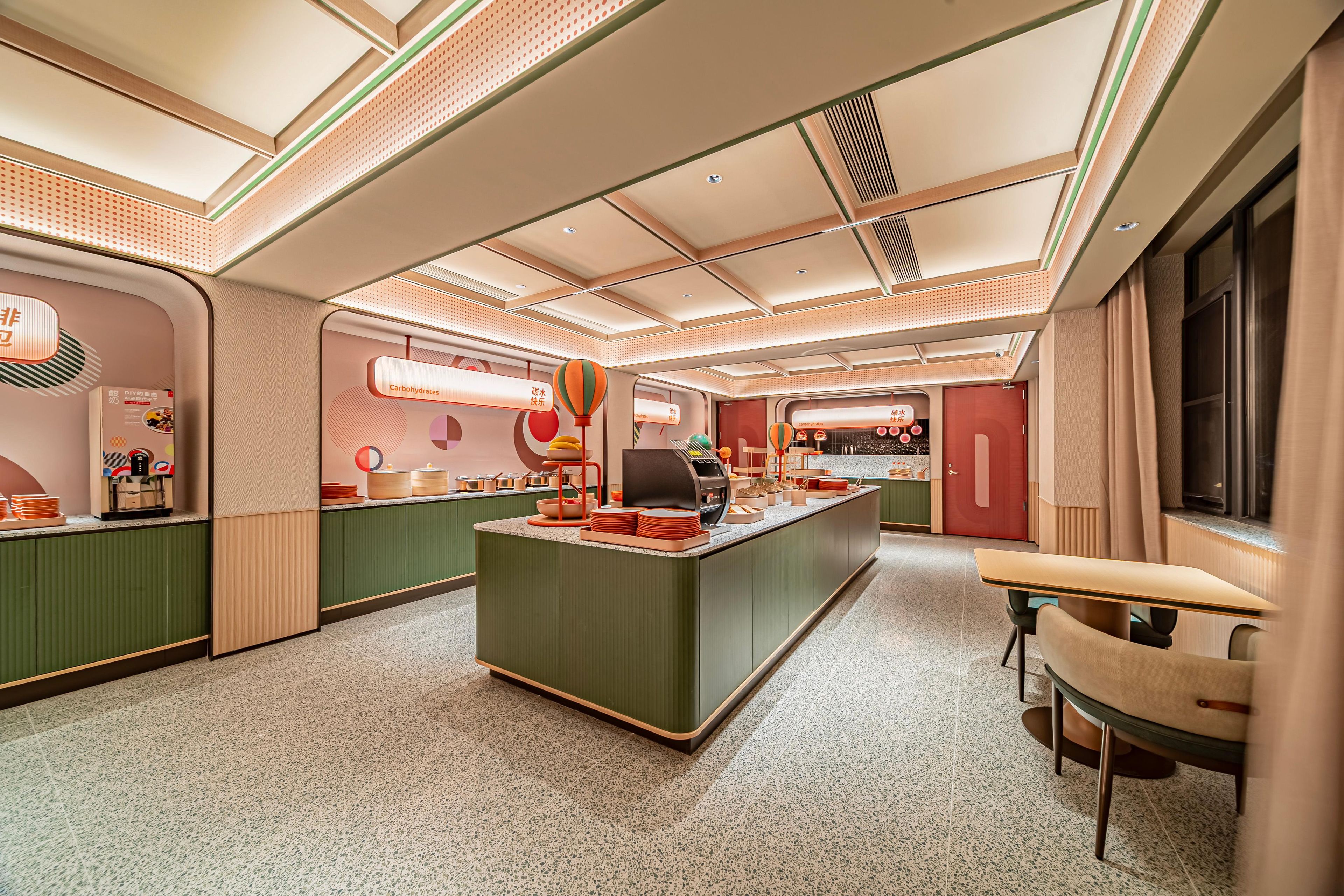 Un área de cocina moderna con una isla central, muebles verdes y una zona de estar con mesa y sillas.