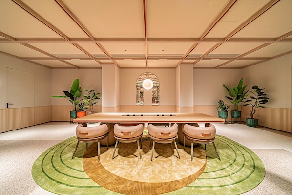 Un salón de conferencias con una larga mesa, seis sillas y un espejo decorativo en el centro.