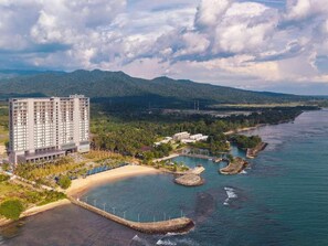 Un hotel frente al mar con playa privada, una construcción grande y montañas al fondo.