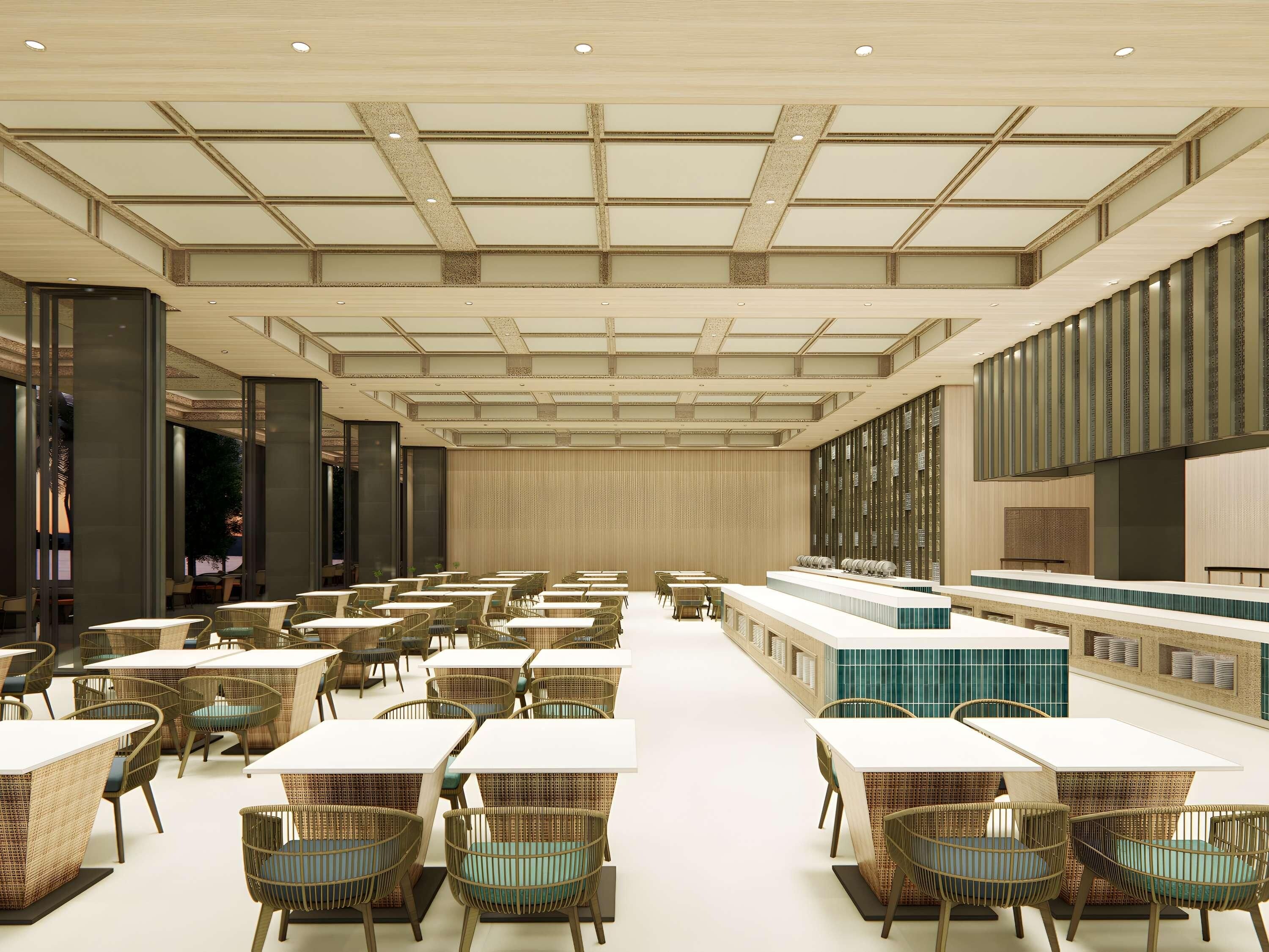 A spacious hotel lobby with high ceilings, a central reception desk, and multiple seating areas with tables and chairs.