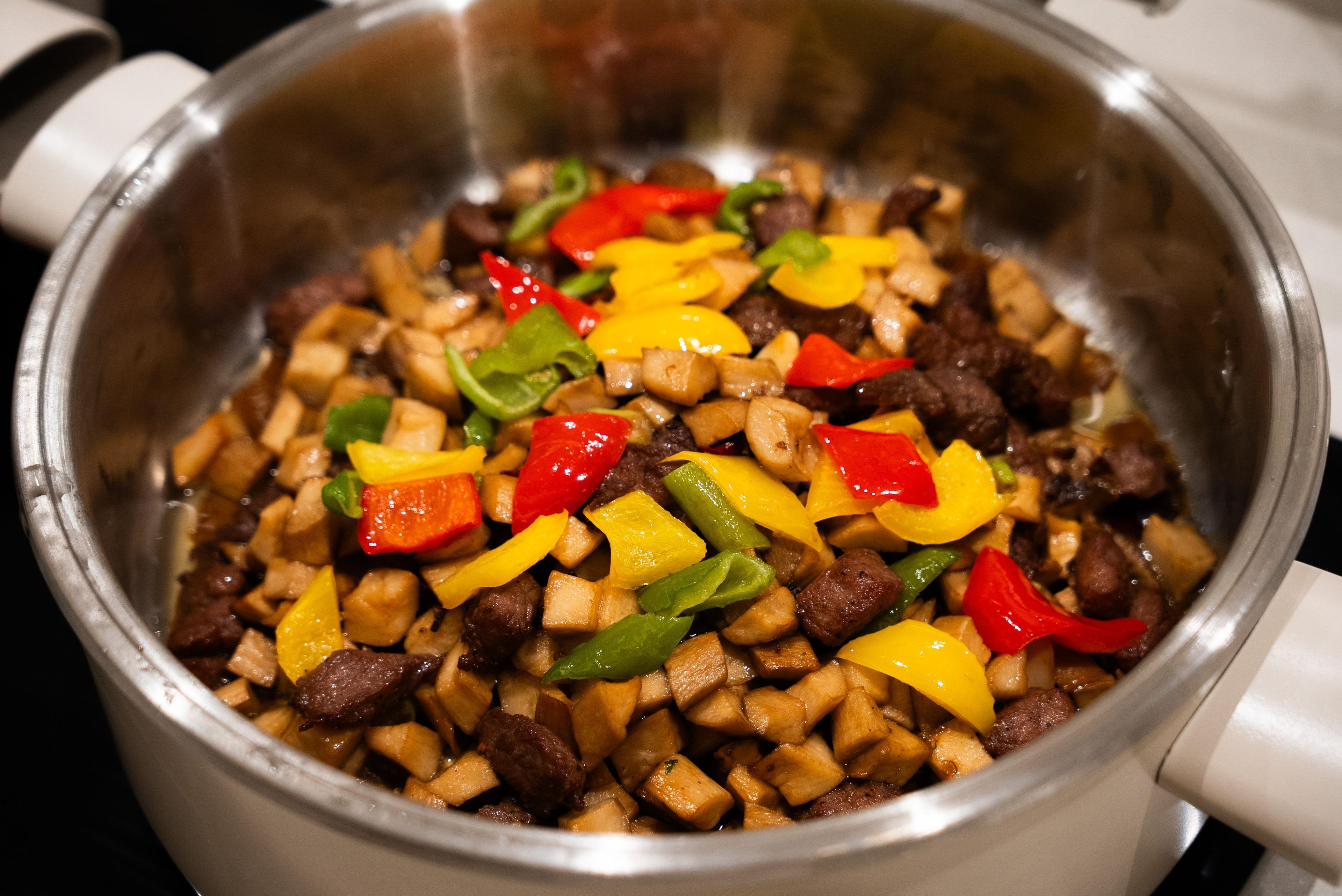 Une casserole en acier inoxydable contenant un plat de légumes et de viande sautés.
