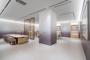 Um interior moderno e minimalista com uma área de estar central, um painel branco grande e uma estante com diversos objetos.