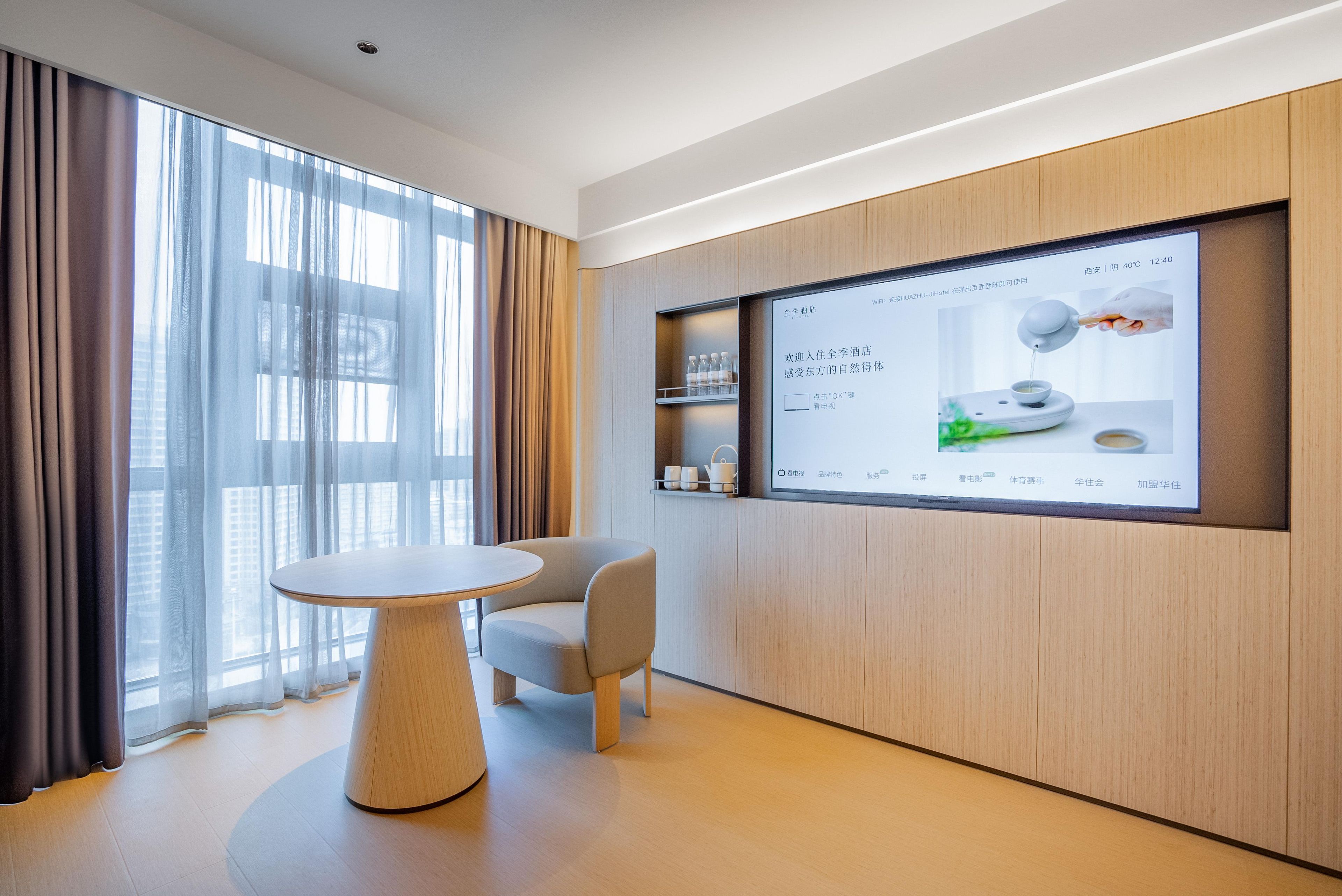 Una habitación de hotel moderna con un gran ventanal, una mesa redonda y una pantalla digital en la pared.