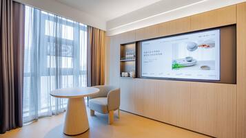 Una habitación de hotel moderna con un gran ventanal, una mesa redonda y una pantalla digital en la pared.