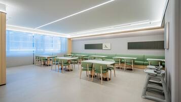 Uma zona de refeições moderna com assentos verdes e mesas brancas, apresentando um design limpo e minimalista.