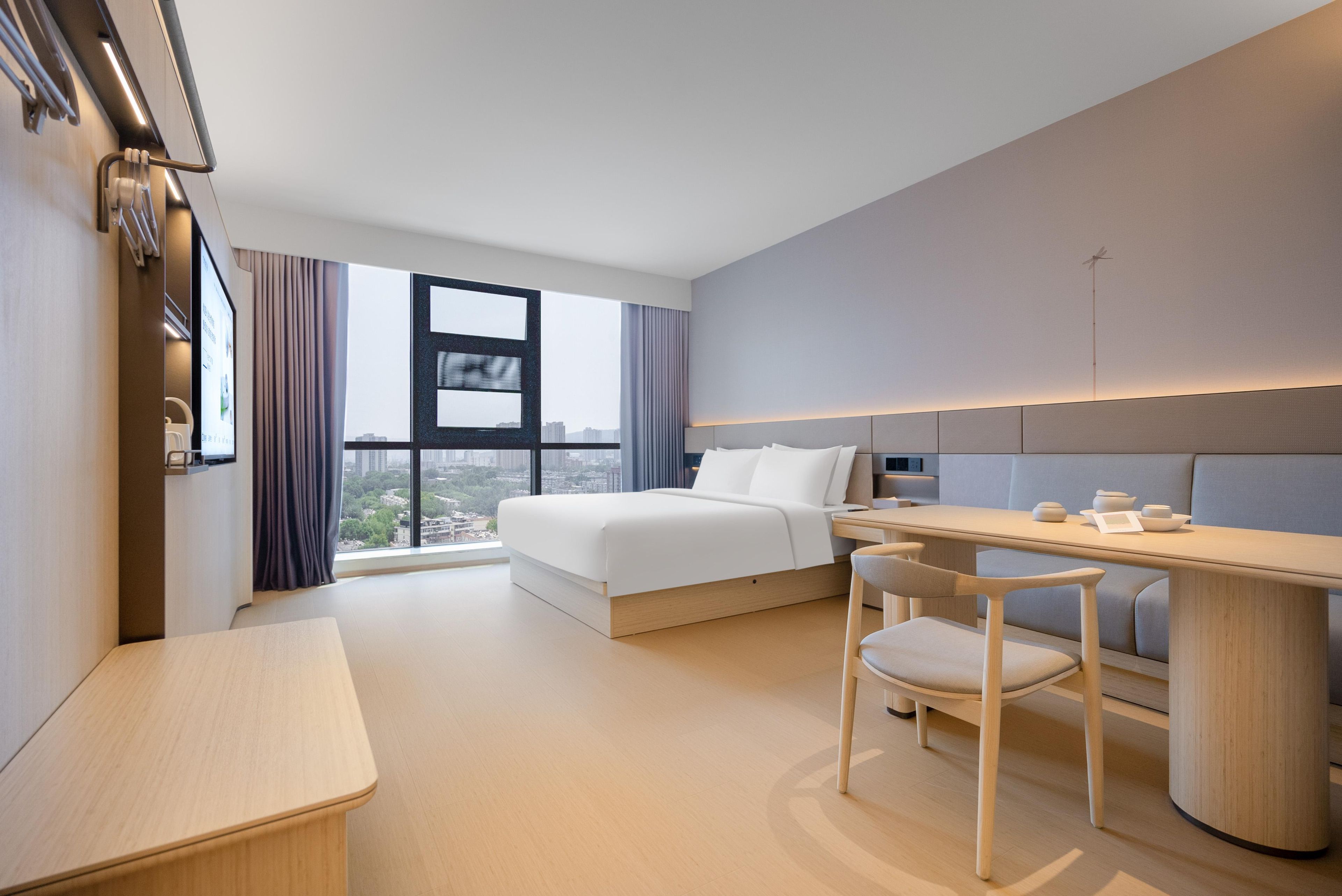 Habitación de hotel moderna con cama, escritorio, silla y vistas de la ciudad a través de amplios ventanales.