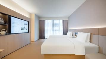 A hotel room with a large bed, a television on the wall, and a window with curtains.