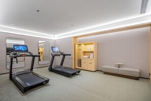 A modern hotel room with two treadmills, a mirror, a small table, and a seating area. - JI Hotel (Xi'an)