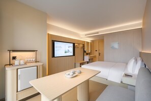 Habitación de hotel con cama, escritorio con computadora, televisor montado en la pared y una pequeña kitchenette.