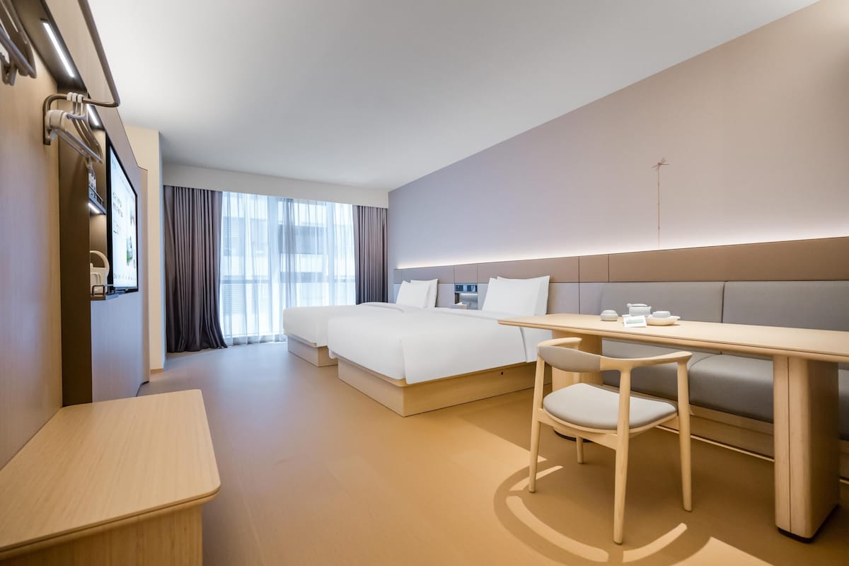 A modern hotel room with a bed, a desk, a chair, and a sofa.
