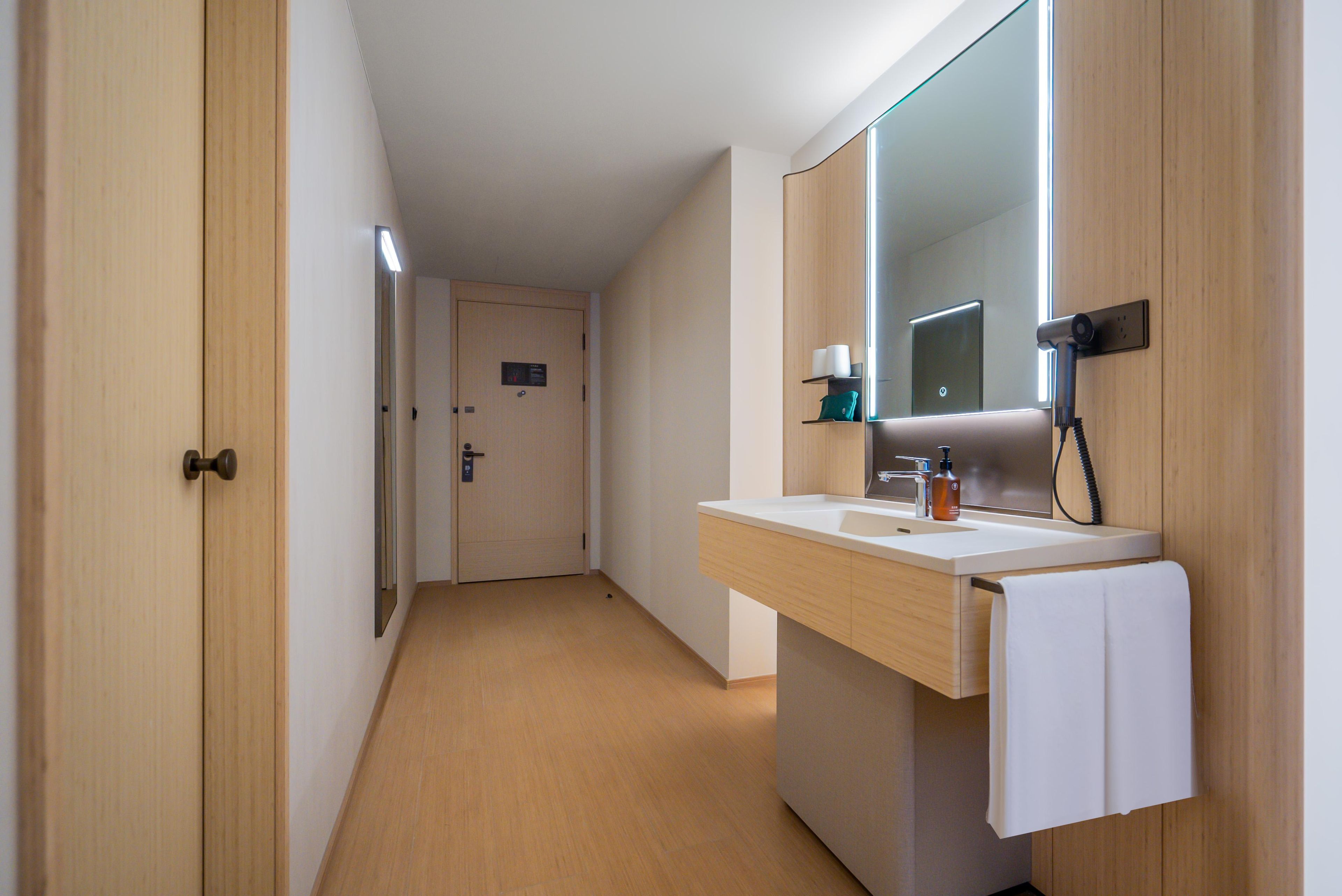 Un baño de hotel con un tocador de madera, un espejo grande y una toalla colgada en la pared.