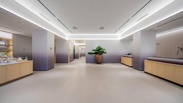 Un moderno vestíbulo de hotel con un mostrador de recepción central, una gran planta en maceta y un largo pasillo que conduce a otras áreas.