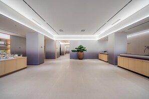 A modern hotel lobby with a central reception desk, a large potted plant, and a long corridor leading to other areas. - JI Hotel (Xi'an)