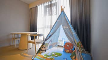 A child's play tent with dinosaur prints, a round table, and a chair in a room with large windows and curtains.
