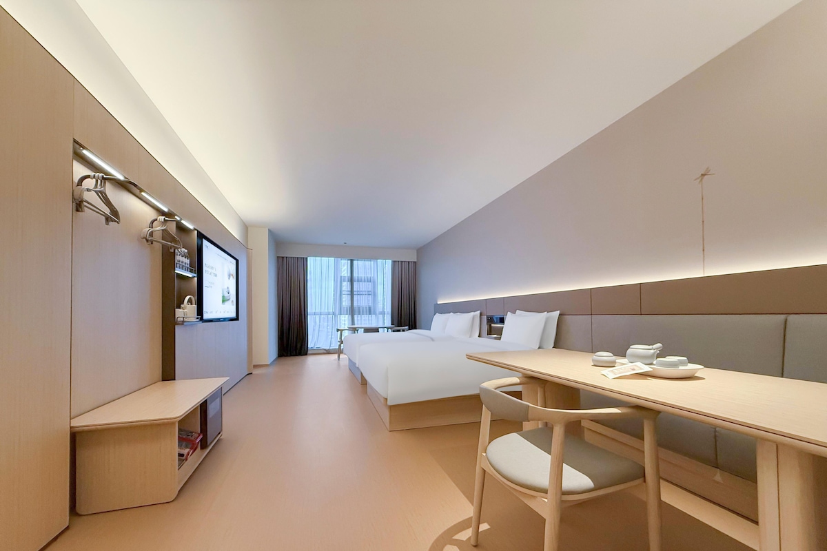 A hotel room with a bed, bedside table, chair, and a TV mounted on the wall.